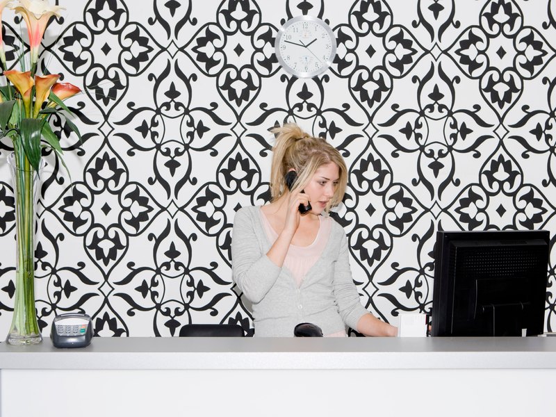 Receptionist in a grey uniform behind the counter holding a cordless phone