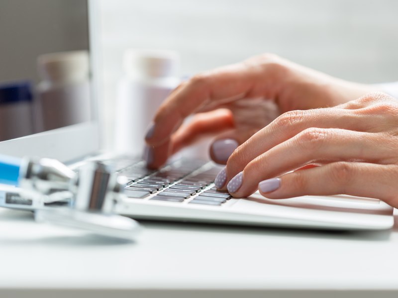 A professional's hands typing on a laptop next to a dental model