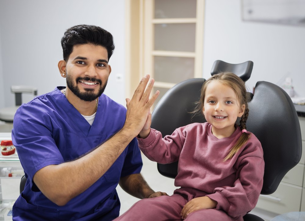 Dentista chocando la mano con una niña en el sillón dental