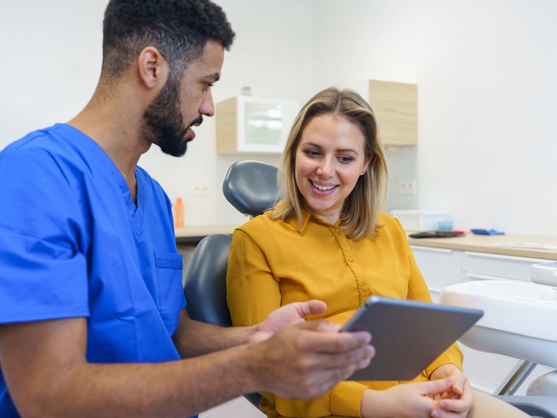 Dentista enseñando en una tableta el diseño de sonrisa a una paciente