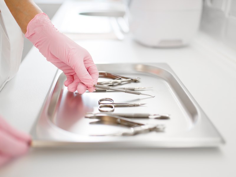 Hand in a pale pink glove picking dental instruments off a metal tray