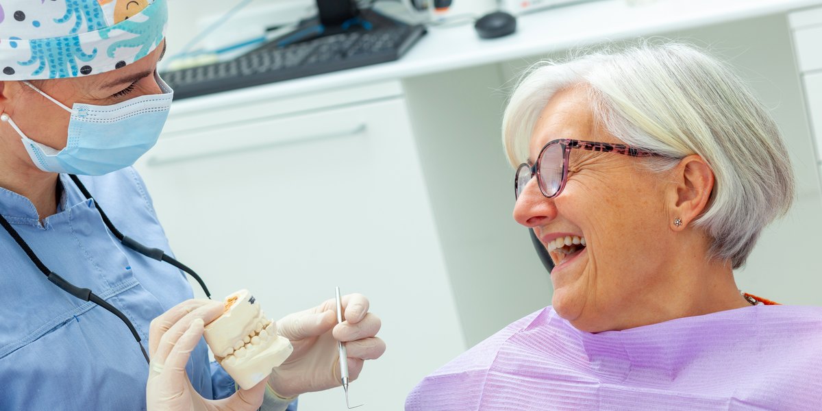 Dentista enseñando a una paciente un modelo dental con la pieza que sustituirá al diente que falta