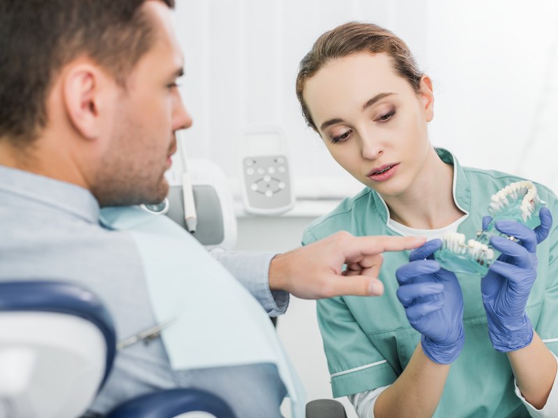 Dentista mostrando a un paciente el modelo de un implante dental en la consulta