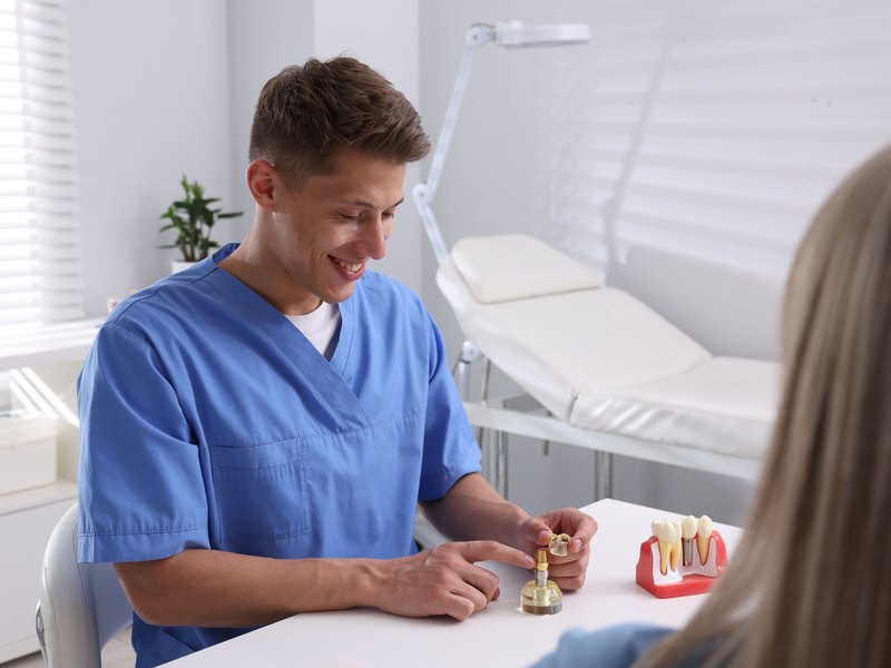 Dentista mostrando a un paciente el modelo de un implante dental en la consulta