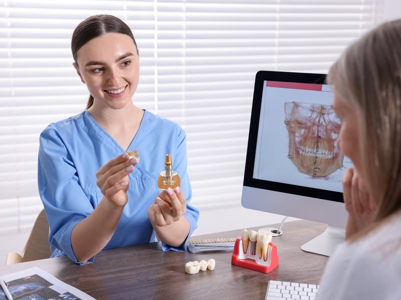 Dentista mostrando a un paciente el modelo de un implante dental en la consulta