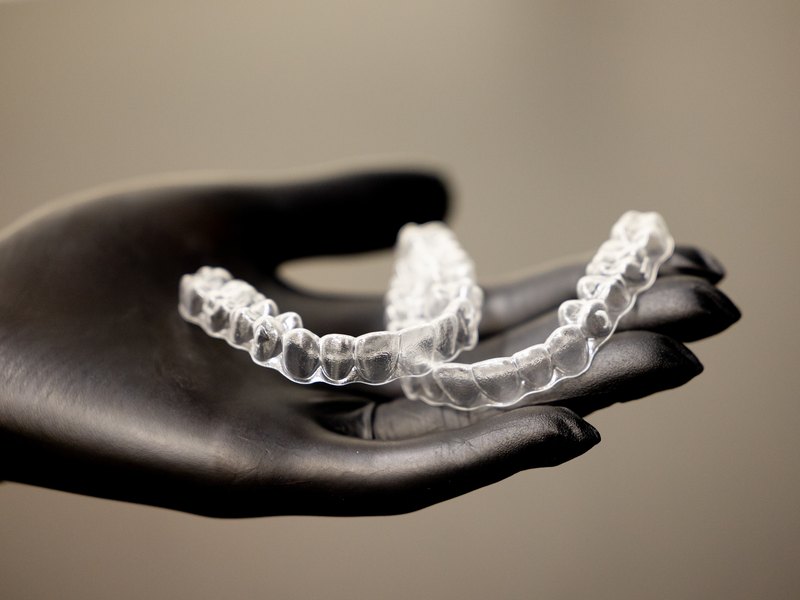 Two dental aligners in a gloved hand on a light beige background