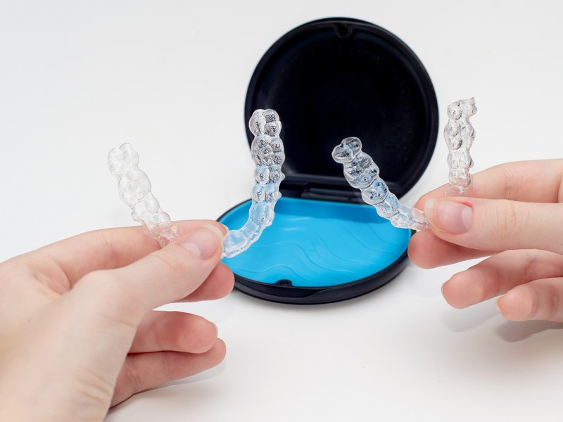 Two hands holding clear aligners with a blue and black storage case