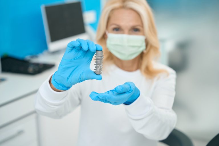 Dentista con mascarilla sosteniendo un implante dental de tamaño reducido