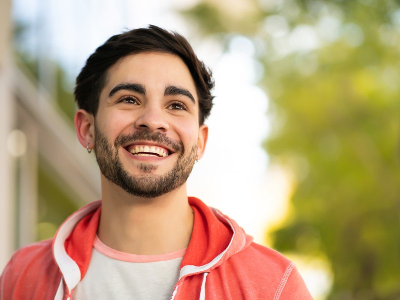 Casual outdoor portrait, man smiling against a blurred green background