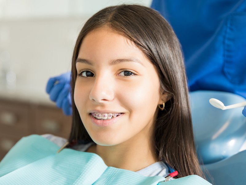 Adolescente con brackets sentada en el sillón dental durante una revisión de ortodoncia