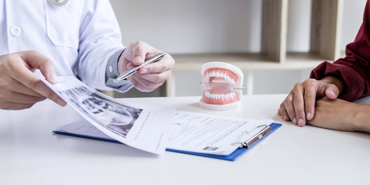 Dentista explicando el presupuesto de un implante dental a un paciente, con la radiografía y el modelo de dientes sobre la mesa