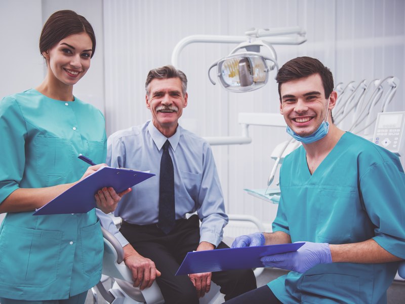 Profesionales con uniforme sanitario en un gabinete dental, junto al sillón y la lámpara
