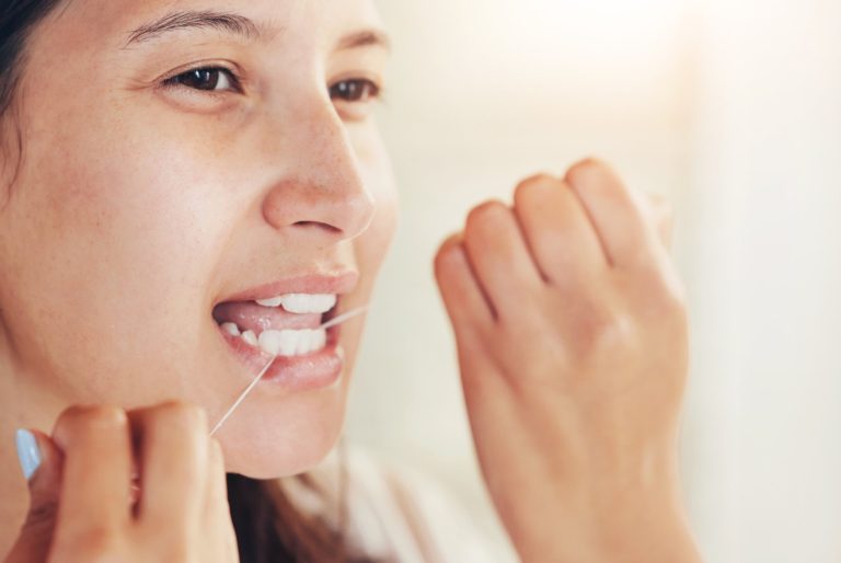 Mujer pasándose el hilo dental entre los dientes frente al espejo