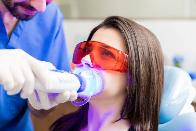 Paciente con gafas protectoras durante un blanqueamiento dental con lámpara en la clínica