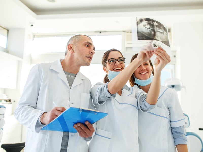 Professional holding a dental x-ray next to two colleagues in blue masks