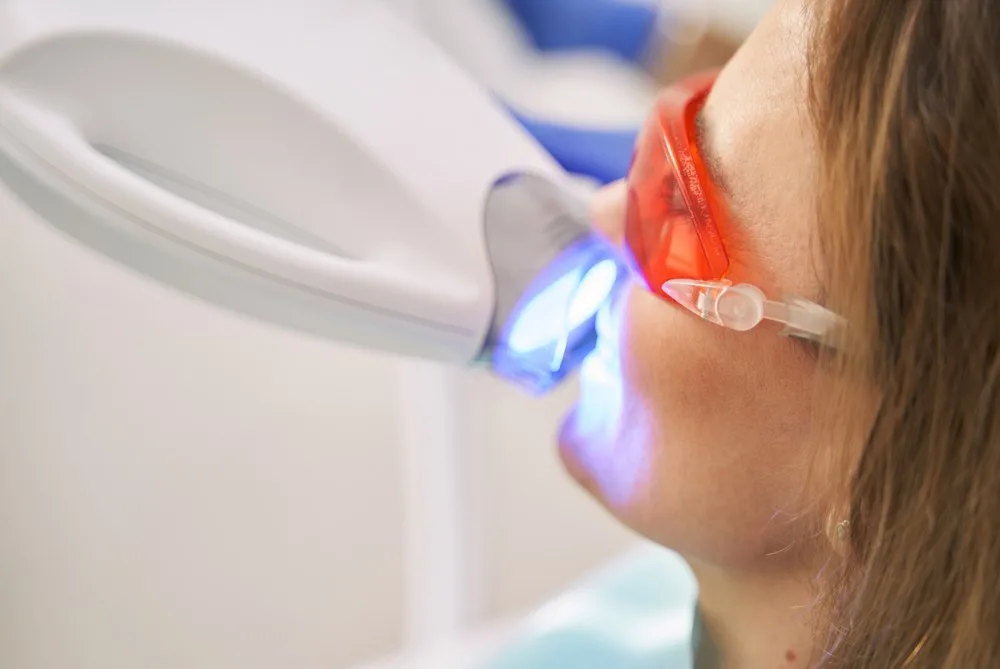 Mujer con gafas protectoras bajo la lámpara de luz azul durante un blanqueado dental en una clínica de Barcelona