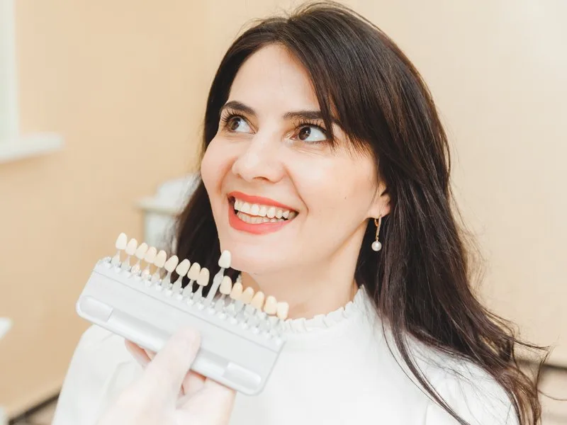 Dona somrient amb una guia de colors dentals per comparar el to abans del blanquejament dental ambulatori