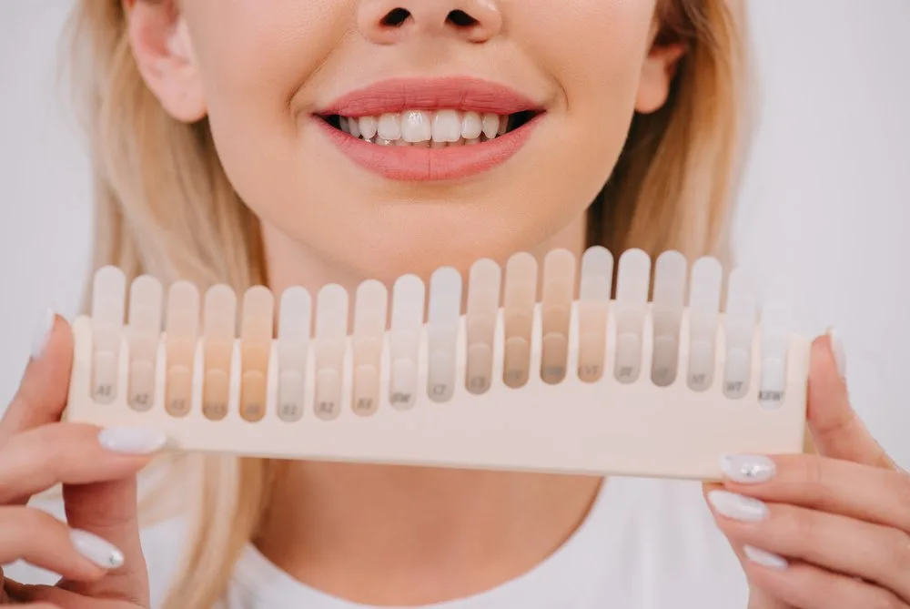 Mujer sonriente sujeta una guía de tonos para elegir el color de sus carillas de composite en Barcelona