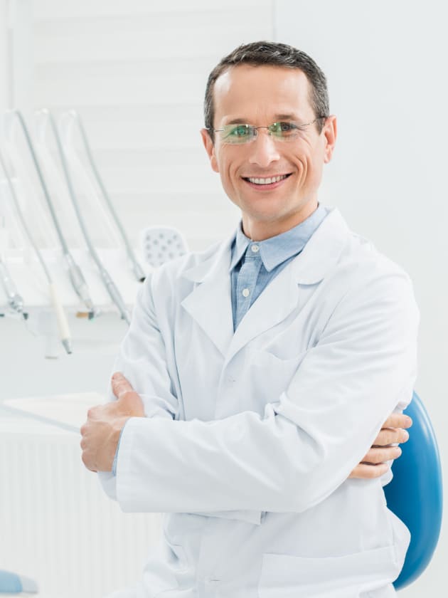 Dentista somrient amb bata blanca i els braços creuats a la consulta