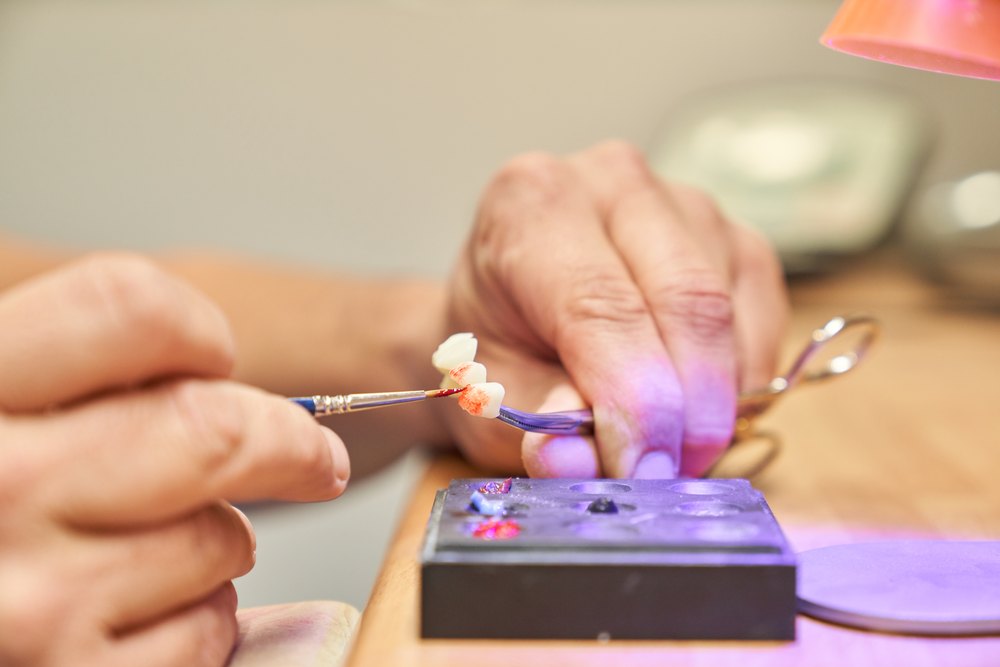 Tècnic dental donant color amb un pinzell a una peça de porcellana al laboratori