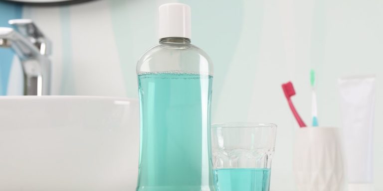 A bottle of mouthwash and a glass next to the sink