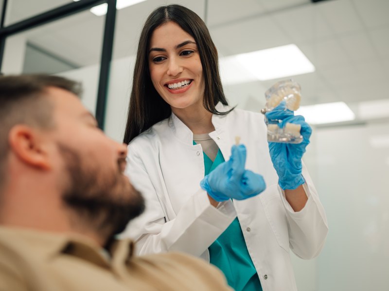 Dentista somrient ensenya un model dental a un pacient abans de la cirurgia guiada