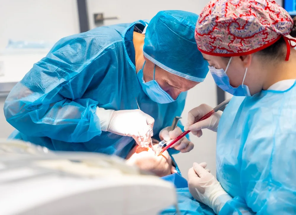 Dentist and assistant in surgical caps and gowns working in a patient's mouth while placing dental fillings in Barcelona