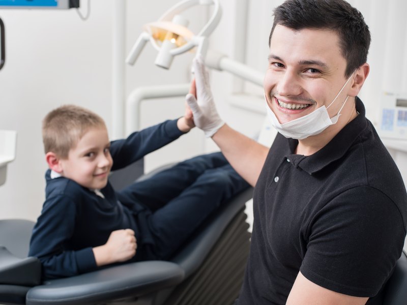 Un nen a la butaca dental amb el dentista somrient al costat