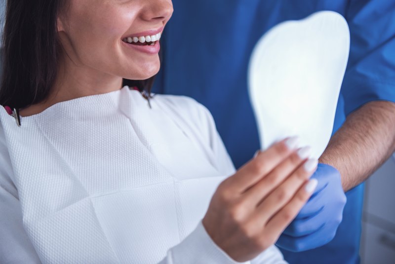 Paciente sonriendo ante el espejo junto al dentista tras un tratamiento de estética dental