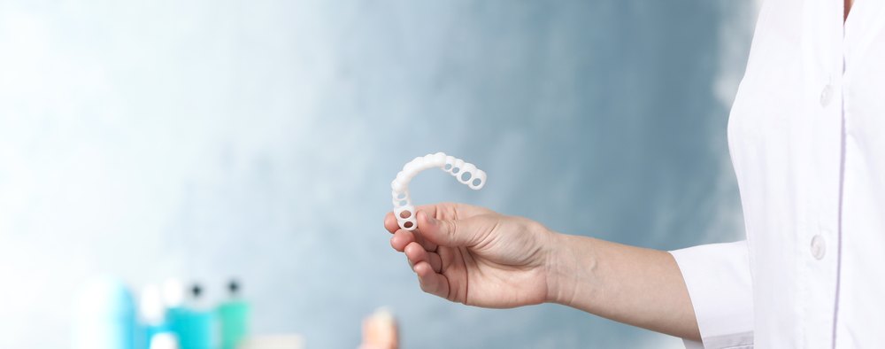 Mà d'un dentista amb bata blanca que sosté un alineador transparent
