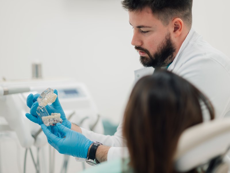 Dentista amb guants blaus subjecta un model d'implant davant d'una pacient