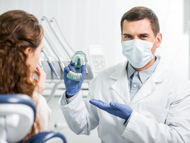 Dentista amb mascareta explica amb un model dental com es col·loca l'implant