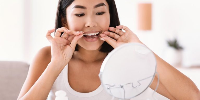 Dona fent servir fil dental davant d'un mirall per cuidar l'alè