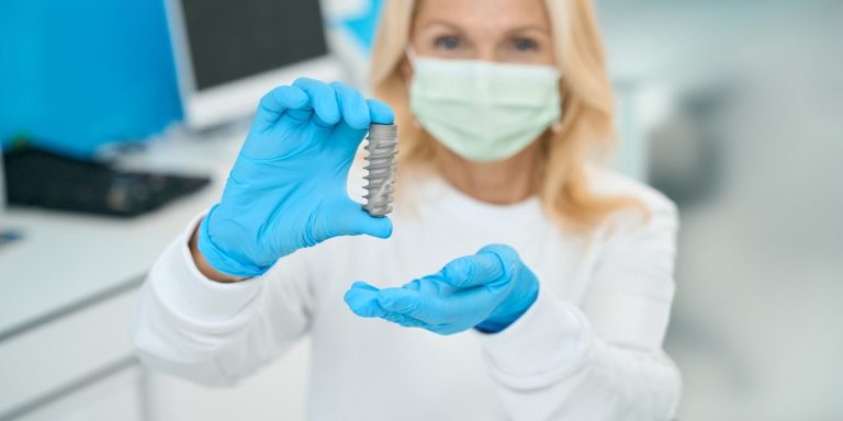 Dentista amb mascareta sostenint un implant dental de mida reduïda