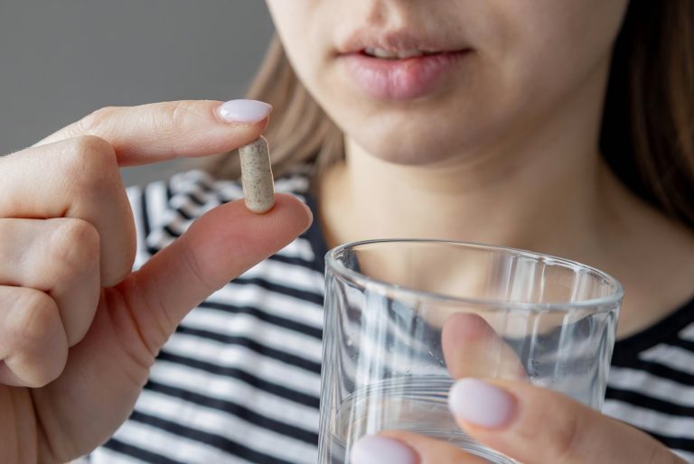 Woman about to take a capsule with a glass of water in her other hand