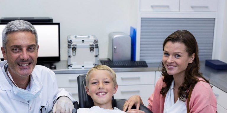 Smiling boy in the dental chair with the dentist and his mother at his side