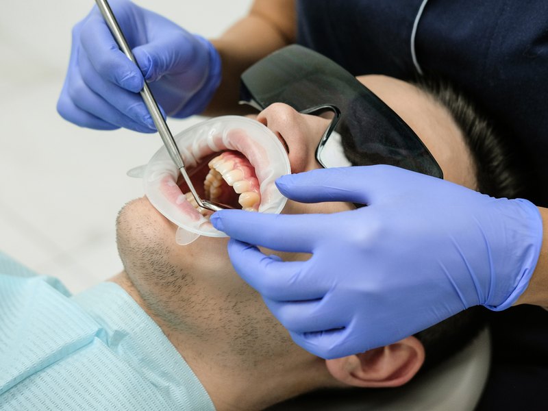 Paciente reclinado con separador de labios mientras se le explora la encía con una sonda dental