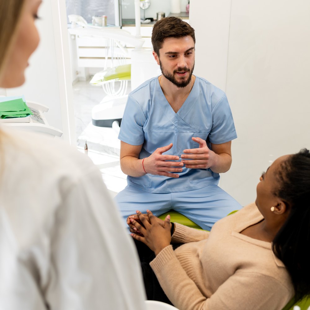 El dentista, assegut, explica a una pacient les opcions del seu pla de tractament