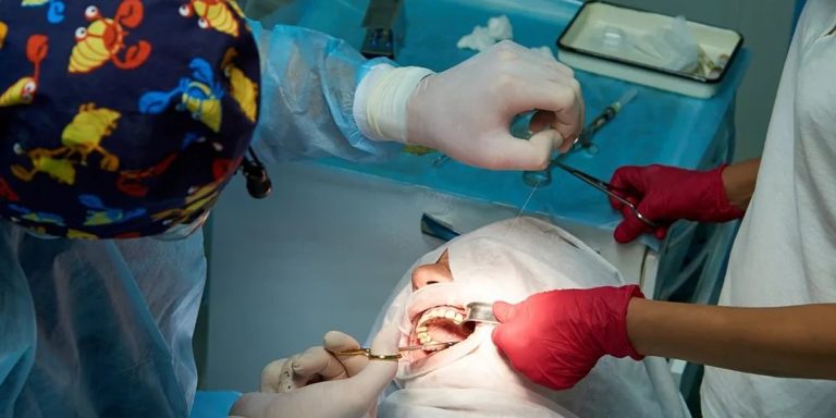Cirugía de encía en el sillón dental: el cirujano da un punto de sutura mientras la asistente separa el labio del paciente