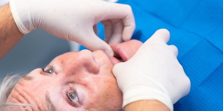 Dentista amb guants separa el llavi d'un pacient gran recolzat a la cadira per revisar-li les genives