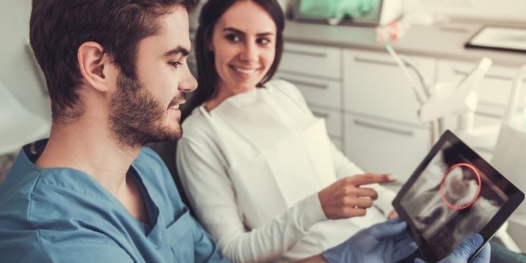 Dentista ensenya en una tauleta una radiografia dental a una pacient somrient que l'assenyala amb el dit