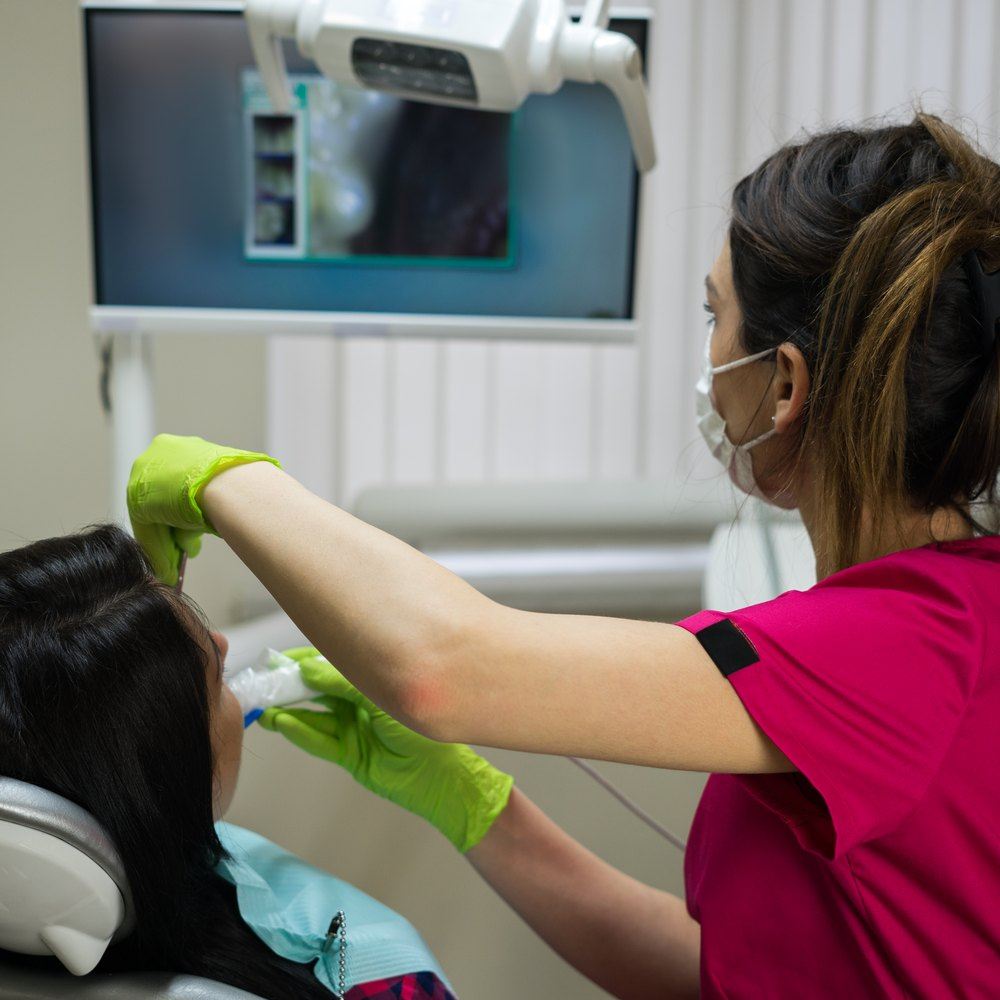 La dentista revisa la boca d'una pacient a la butaca, amb la pantalla de la càmera intraoral al darrere
