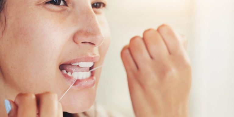 Dona passant-se el fil dental entre les dents davant del mirall