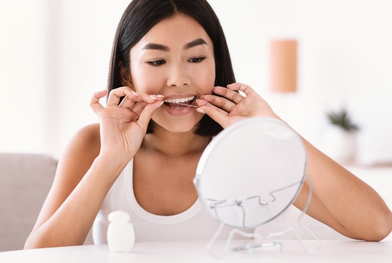 Mujer usando hilo dental frente a un espejo para cuidar su aliento