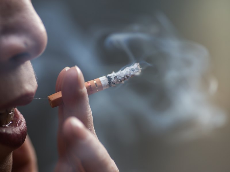 Persona amb una cigarreta encesa als llavis mentre treu el fum