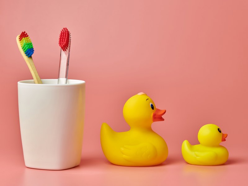 Vaso con dos cepillos de dientes junto a dos patitos de goma sobre un fondo rosa