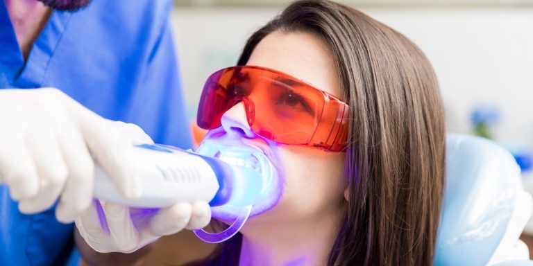 Pacient amb ulleres protectores durant un blanquejament dental amb làmpada a la clínica